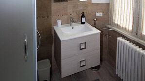 A bathroom with a white sink, a mirror, a radiator, and a window with curtains. - La finestra sul Pincio, Appartamento a due passi dalla stazione e dal porto. (Civitavecchia)