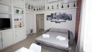 A modern hotel room with a bed, a TV, a white wardrobe, and a wine collection on shelves. - La finestra sul Pincio, Appartamento a due passi dalla stazione e dal porto. (Civitavecchia)