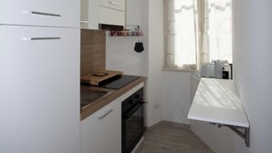 A compact kitchen with white cabinets, a wooden countertop, and a window with sheer curtains. - La finestra sul Pincio, Appartamento a due passi dalla stazione e dal porto. (Civitavecchia)