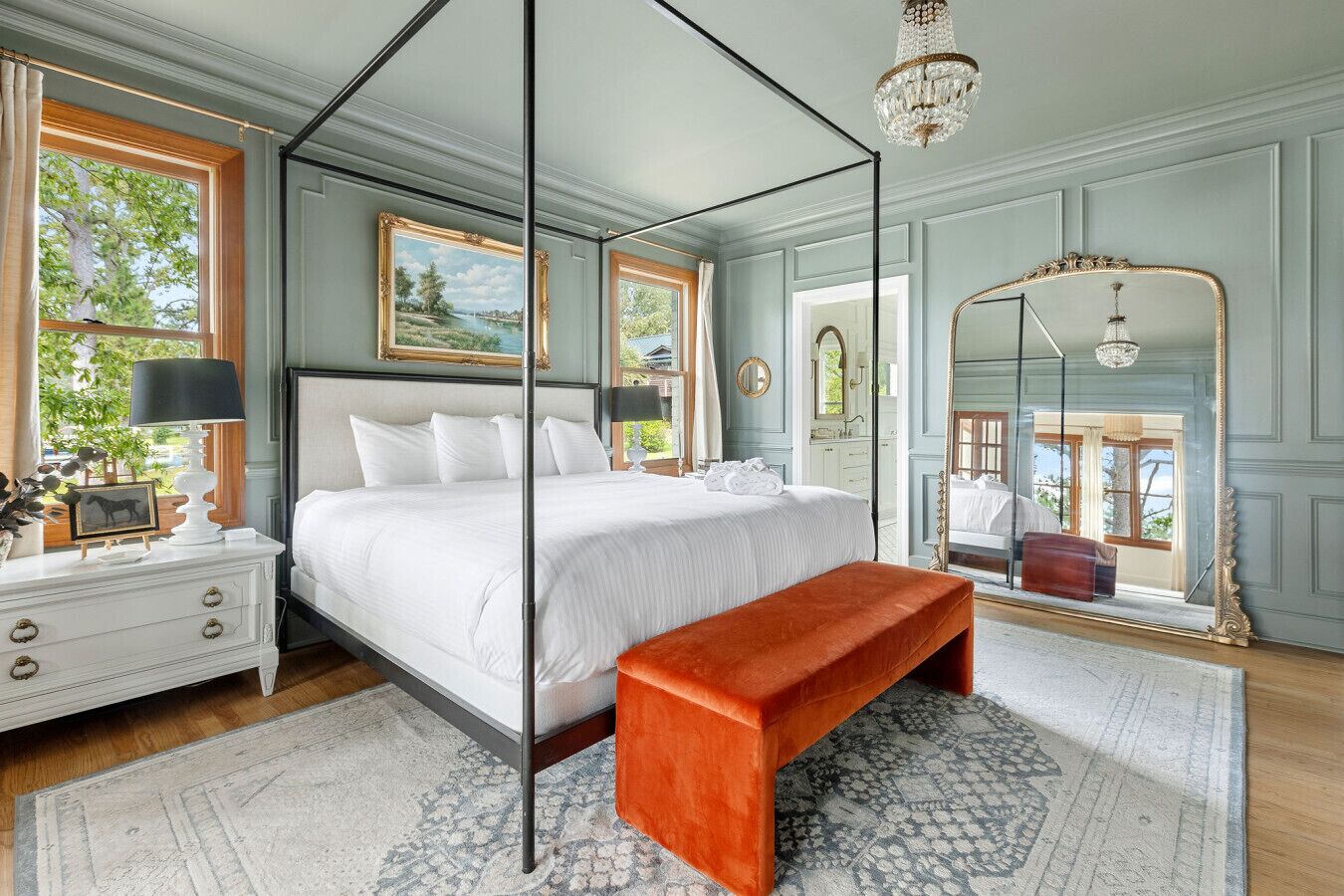A four-poster bed with a white canopy, a wooden bench, a white dresser, and a large mirror.