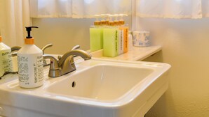 A bathroom sink with a hand soap dispenser, a faucet, and a shelf with various toiletries. - Dew Duck Inn (Plains)