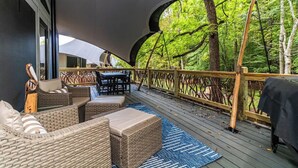 Eine Terrasse im Freien mit Korbmöbeln, einem Tisch und Stühlen, umgeben von einem Holzgeländer und Bäumen.