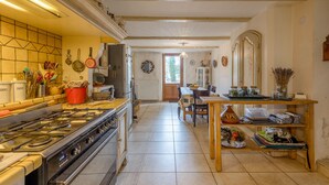 A kitchen with a stove, cabinets, and a dining area with a table and chairs. - Le Guiguet - Mas provençal avec piscine pour 10 (Vedene)