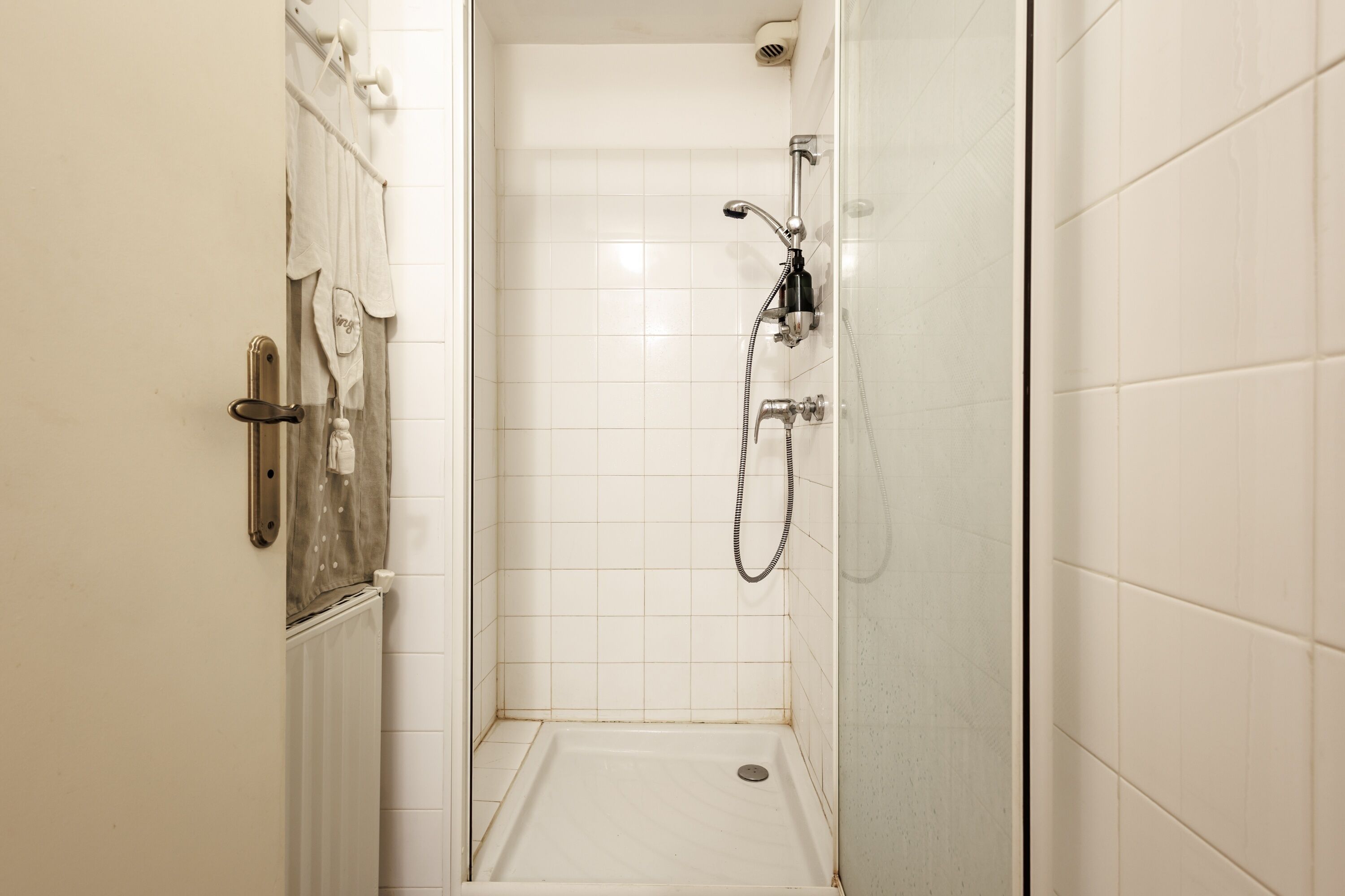 A small, enclosed shower area with a glass door, white tiled walls, and a showerhead.