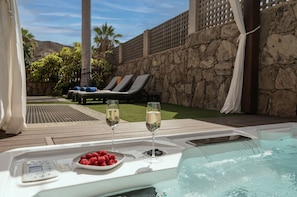 A hot tub with a control panel, two glasses of champagne, and a plate of raspberries.