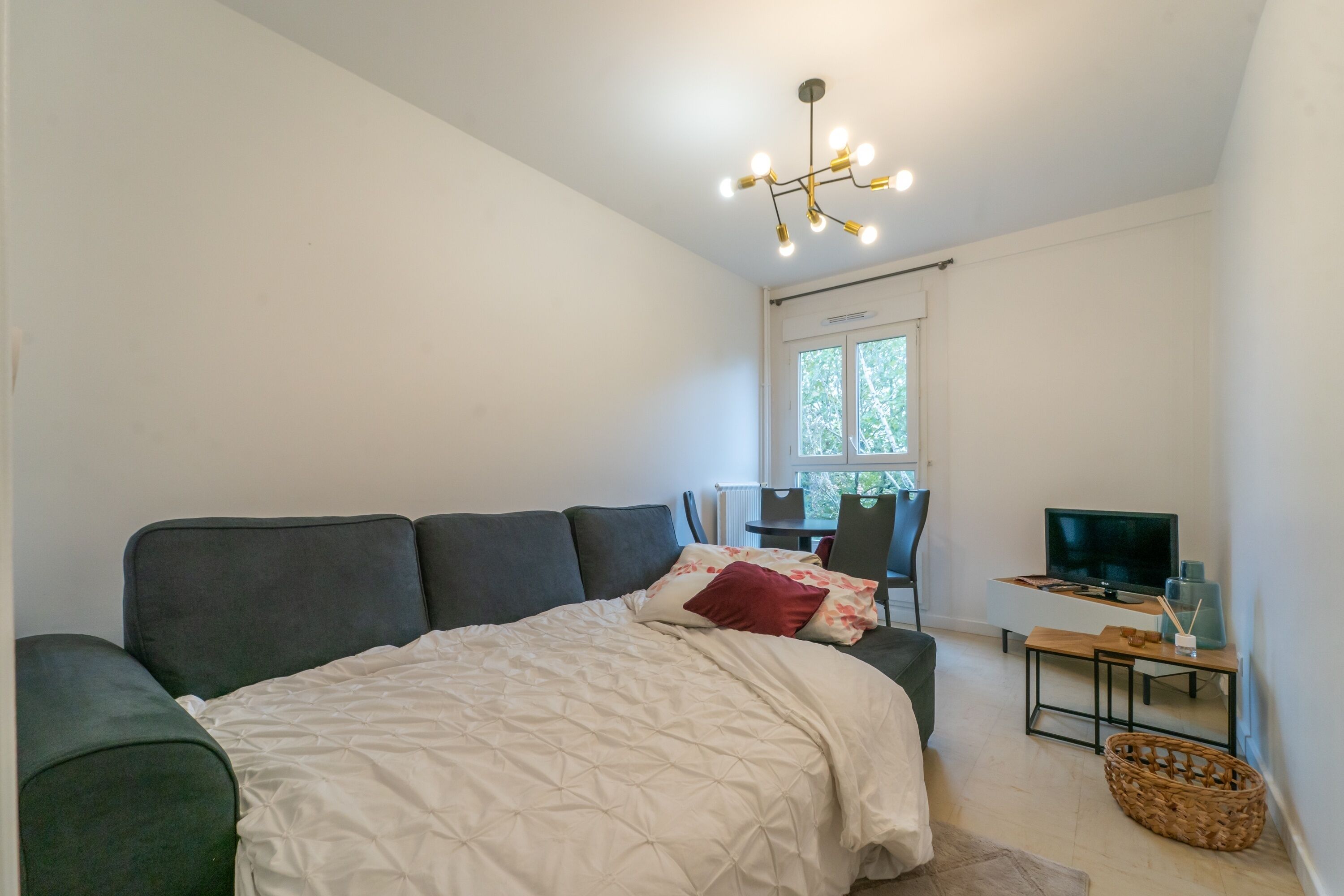 A bedroom with a bed, a desk with a TV, and a window.