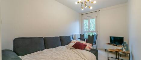 A bedroom with a bed, a desk with a TV, and a window.