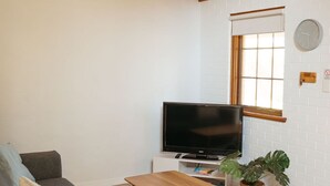 A living room with a sofa, a coffee table, a flat-screen TV, a potted plant, and a window with a view. - Langmeil Cottages - Blue Gum (Tanunda)