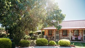 A rustic stone building with a red roof, surrounded by well-maintained hedges and a gravel driveway. - Langmeil Cottages - Blue Gum (Tanunda)