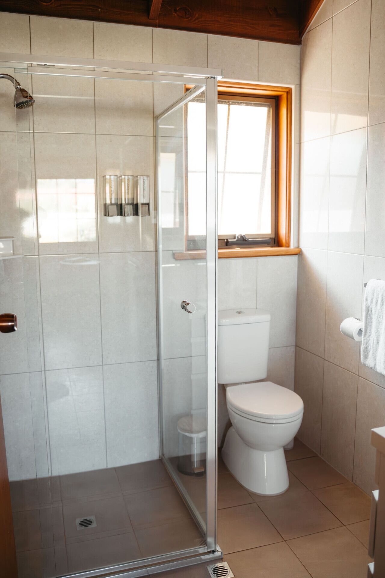 A bathroom with a glass-enclosed shower, a toilet, and a window above the toilet.