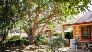 Une maison en pierre dotée d’un espace extérieur couvert, entourée d’une végétation luxuriante et d’un grand arbre.