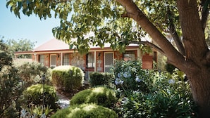 Une maison à deux étages, avec un toit rouge, entourée de jardins bien entretenus et d’un grand arbre.
