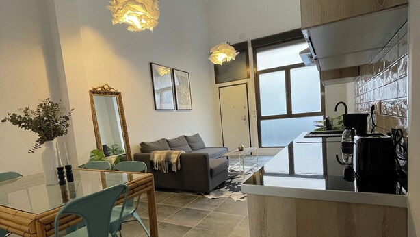Una sala de estar moderna con una mesa de comedor de vidrio, un sofá y una cocina con estufa y lavaplatos.