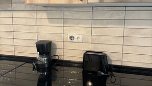 Una cocina con armarios de madera, un microondas negro, una cafetera y un tostador sobre una encimera negra.