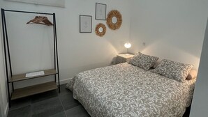 Un dormitorio con una cama, una mesita de noche, un estante en la pared y una ventana.