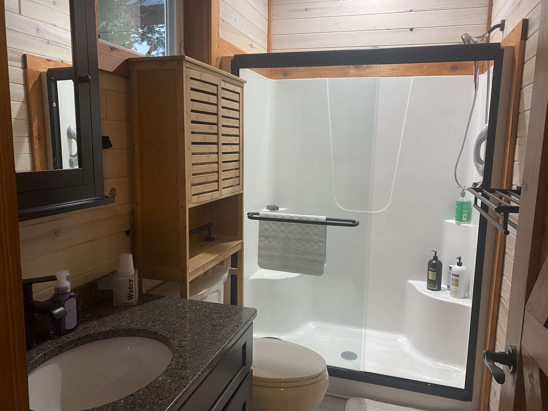 A bathroom with a glass-enclosed shower, a toilet, a sink, and wooden cabinetry.