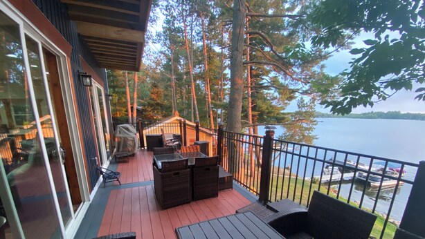 A deck with wicker furniture, a covered grill, and a view of the lake. - Spacious Lakefront Cabin Sleeps up to 14. (Hatley)