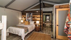 Une chambre à coucher comprenant un lit, des lampes de chevet, une tête de lit en bois, un tapis et une porte donnant sur une autre pièce.