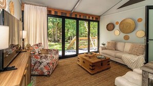 Un salon avec un canapé, une table basse et un téléviseur. Une grande fenêtre offre une vue sur l’extérieur.