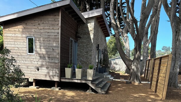 Une cabane rustique avec des fondations en pierre, un revêtement extérieur en bois et une petite véranda agrémentée de plantes en pot.