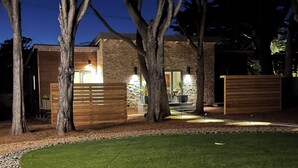 Une maison moderne avec une façade en pierre, une terrasse en bois et une pelouse bien entretenue.