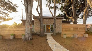 Un chemin de pierres mène à une maison moderne, entourée d’une clôture en bois et d’arbres.