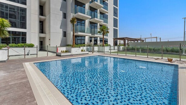 Um hotel moderno com uma grande piscina ao ar livre, rodeada por um deck de madeira e palmeiras.