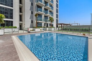 Et moderne hotel med en stor udendørs swimmingpool, omgivet af en træterrasse og palmer.