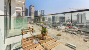 Uma varanda com uma mesa de madeira, um vaso com flores e vista para o horizonte urbano com edifícios e guindastes.