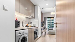 A modern kitchen with built-in appliances, a dining area with a grey sofa, and a view of the city through large windows. - Charming Chalet Escape (Dubai)