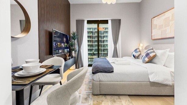 A modern hotel room with a bed, a desk with a chair, a television, and a view of the city through the window. - Charming Chalet Escape (Dubai)
