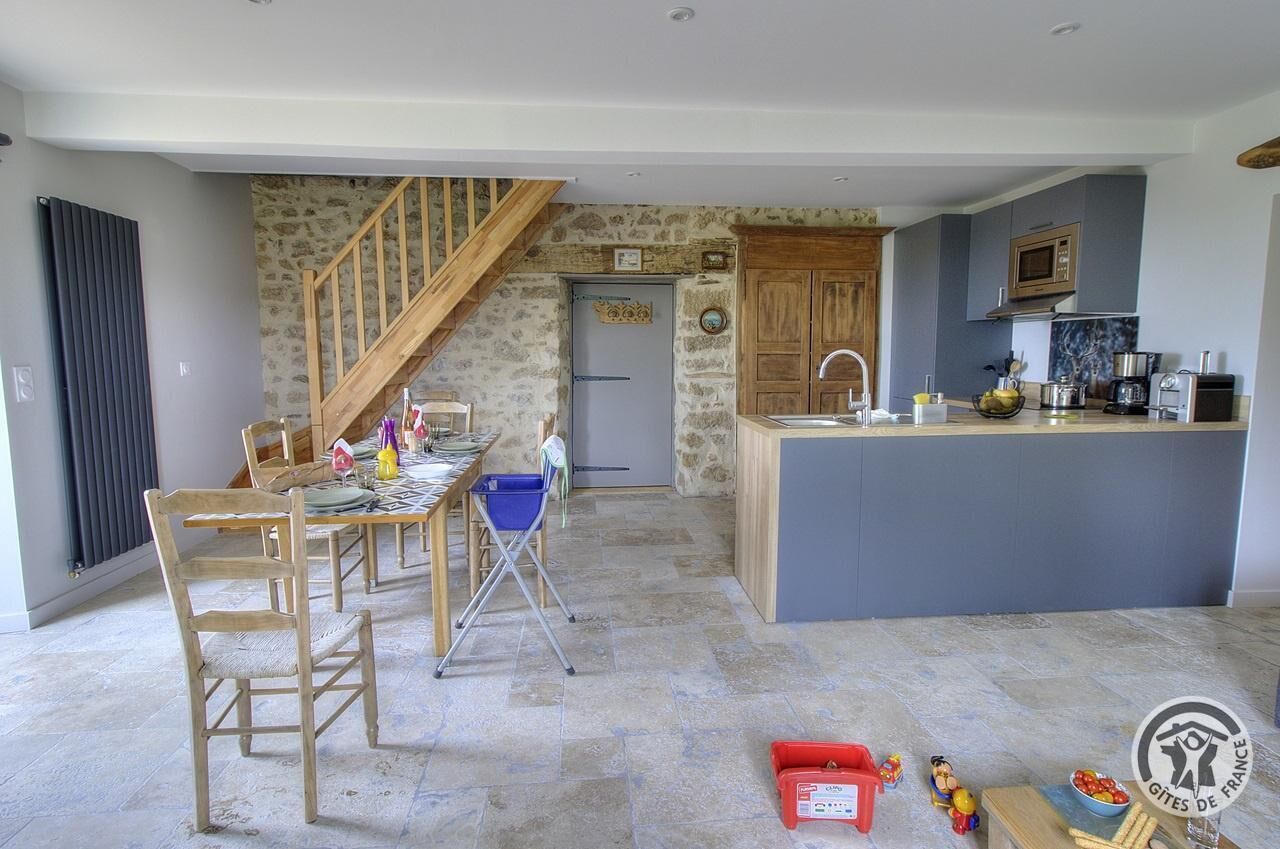 A spacious kitchen with a central island, a dining area with wooden chairs, and a staircase leading to another level.