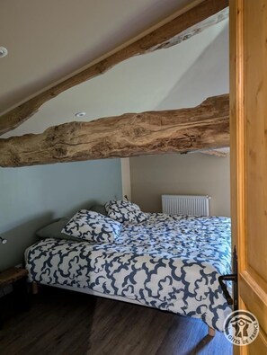 Une chambre avec un plafond en pente, des poutres apparentes, un lit avec une literie à motifs, un radiateur et un banc en bois.