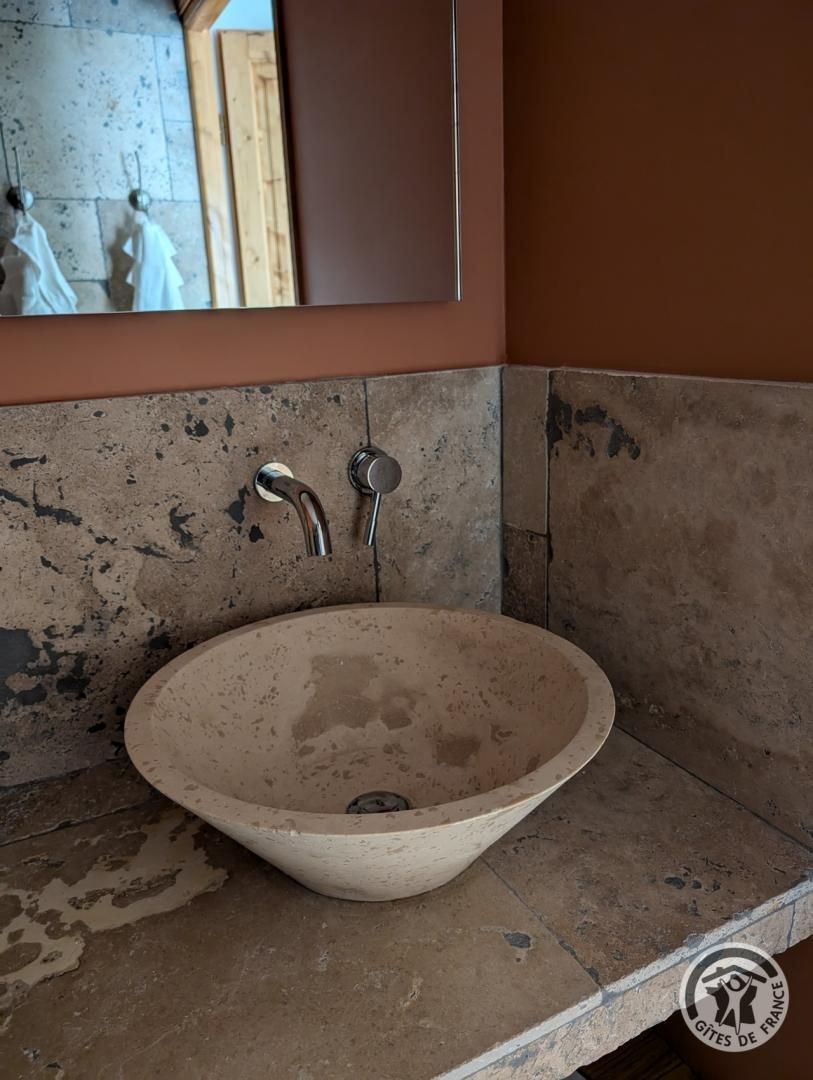A bathroom with a beige ceramic sink, two faucets, and a mirror above.