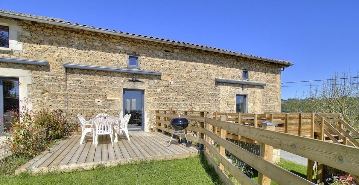 Un bâtiment en pierre doté d’une terrasse en bois, d’un barbecue et de mobilier d’extérieur.