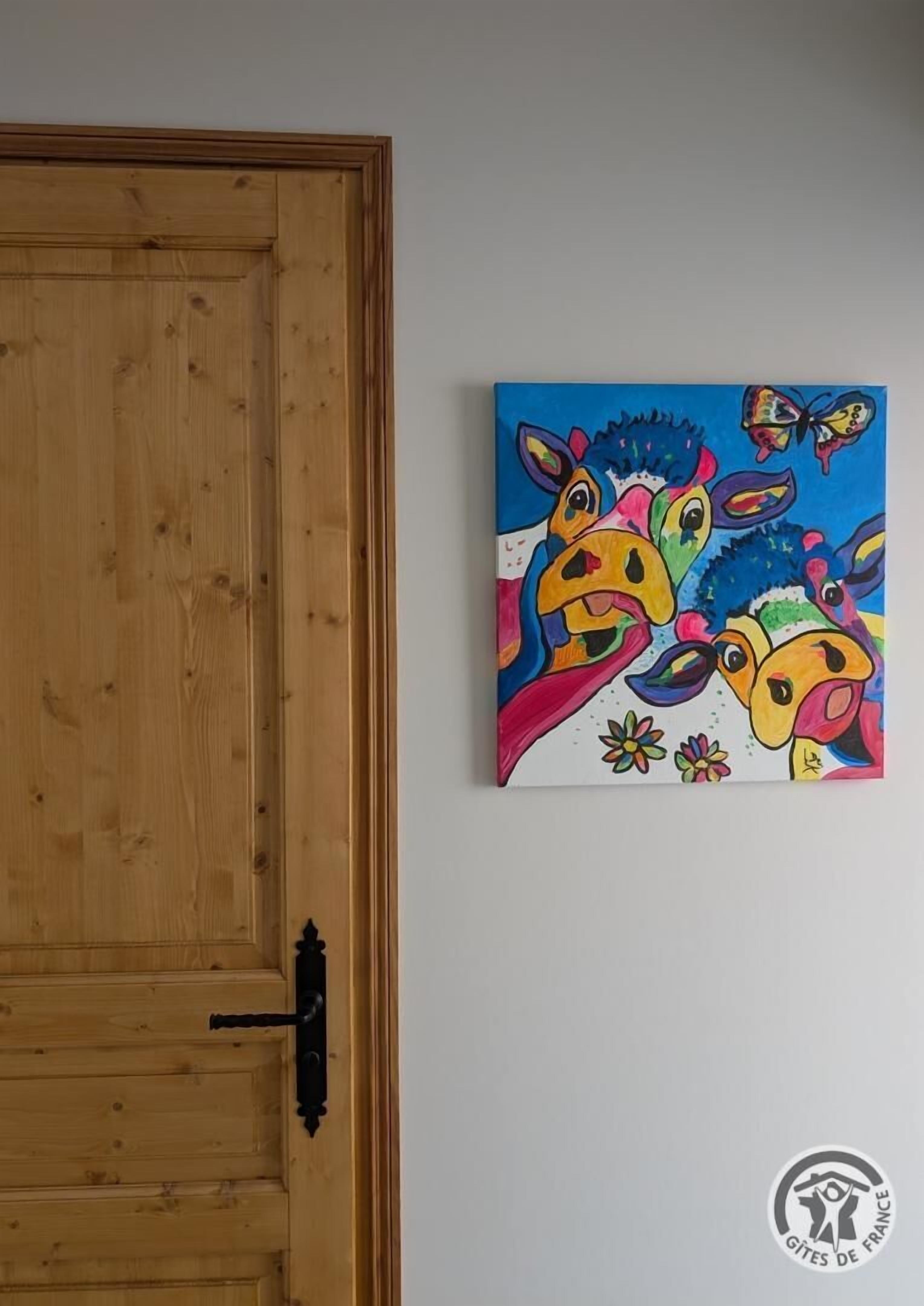 Eine Holztür mit schwarzem Griff und einem farbenfrohen Gemälde von abstrakten Gesichtern und Schmetterlingen an der Wand.