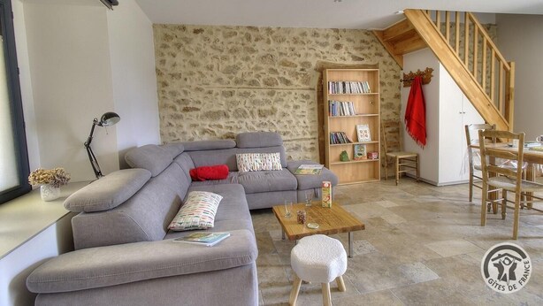 Ein Wohnzimmer mit grauem Sofa, einem Holztisch, einem Bücherregal und einer Treppe.