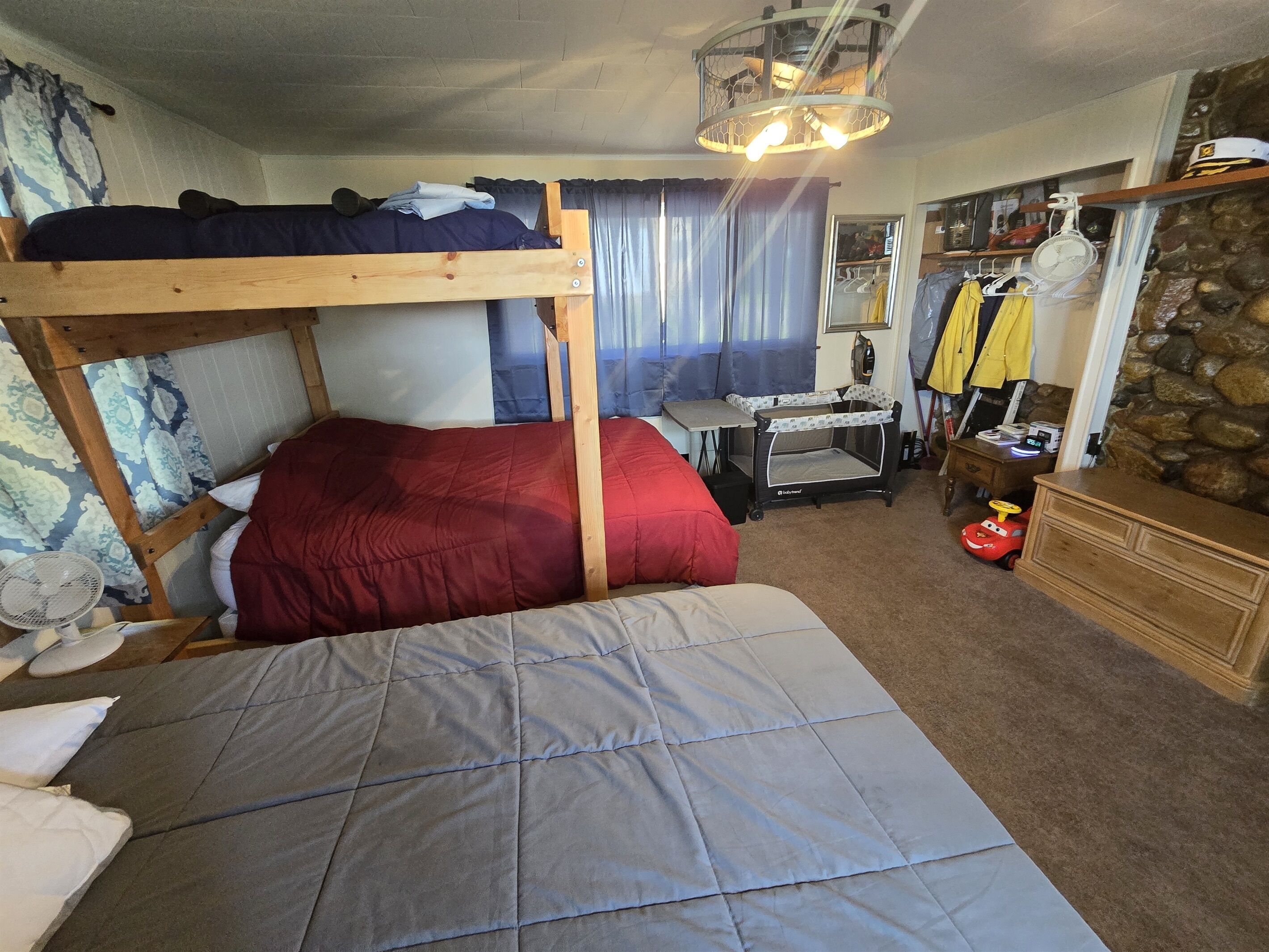 A room with a bunk bed, a desk, a chair, a baby crib, and a dresser.