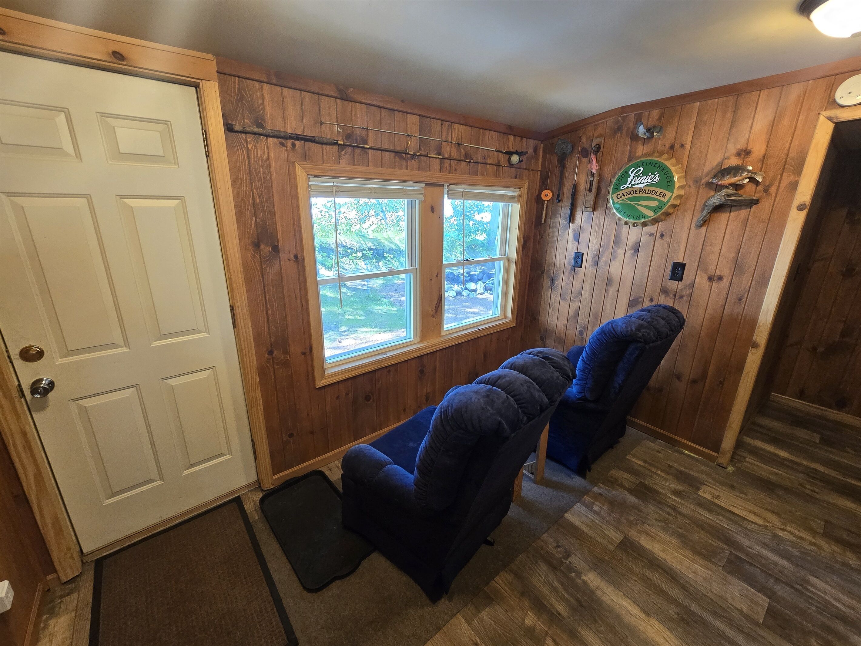 A room with wooden walls, a white door, and a window. There are two blue chairs and a small rug on the floor.