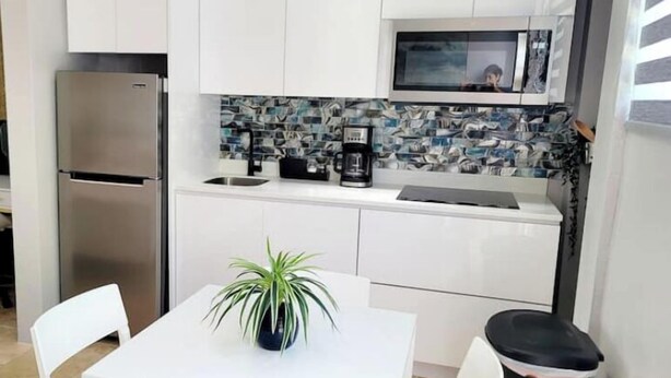 A compact kitchen with white cabinets, a stainless steel refrigerator, a microwave, a sink, and a small dining table with chairs. - Mountain (Sky Sun Villas)

 (Luquillo)