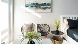Un salon moderne avec un canapé blanc, un fauteuil noir, une petite table sur laquelle est posée une plante, et un tableau accroché au mur.