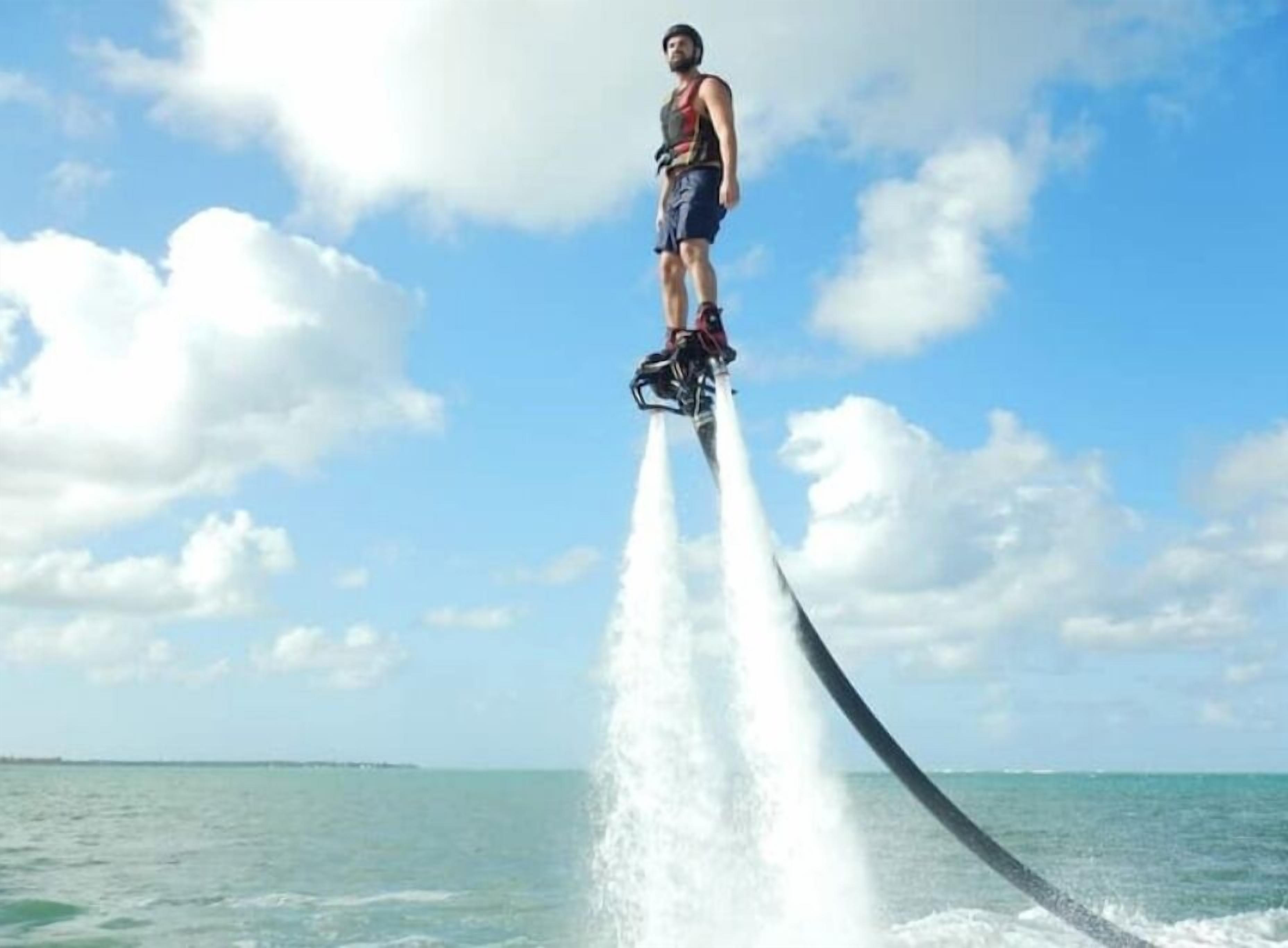 Eine Person fährt mit einem Jetski über ruhiges Wasser an einem klaren Tag, im Hintergrund eine Küstenlinie.