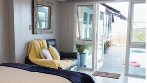 Un dormitorio con cama, una silla, un ventanal y vistas al exterior.