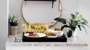 Een witte eettafel met twee gestoffeerde bankjes, een ronde spiegel en een 'Happy Birthday' bord erboven.