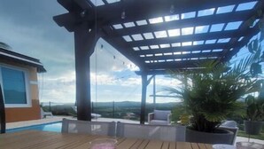 Een houten terras met een tafel, een bord met eten en drinken, en uitzicht op het landschap.