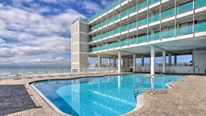 A swimming pool with a clear view of the ocean, a multi-level building with balconies, and a paved deck area. - COUPLES GETAWAY,HONEYMOON SWEET,Beach Front Condo,kitchen,pool,FREE Prkng,GREAT! (Panama City Beach)
