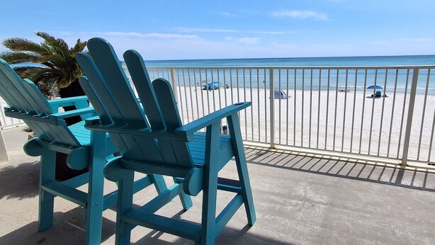 A balcony with turquoise Adirondack chairs overlooking a beach with a white fence. - COUPLES GETAWAY,HONEYMOON SWEET,Beach Front Condo,kitchen,pool,FREE Prkng,GREAT! (Panama City Beach)
