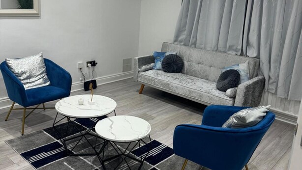 Ein Wohnzimmer mit grauem Sofa, zwei blauen Sesseln, einem weißen Couchtisch und einem Teppich in Grau und Schwarz.