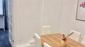 Ein Essbereich mit einem Holztisch, weißen Stühlen und einer Vase mit Trockenblumen.