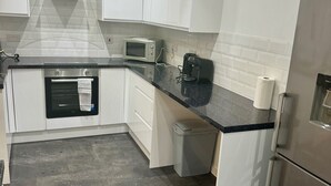 Eine moderne Küche mit weißen Schränken, einem Edelstahl-Kühlschrank, einer Mikrowelle und einer Kaffeemaschine.